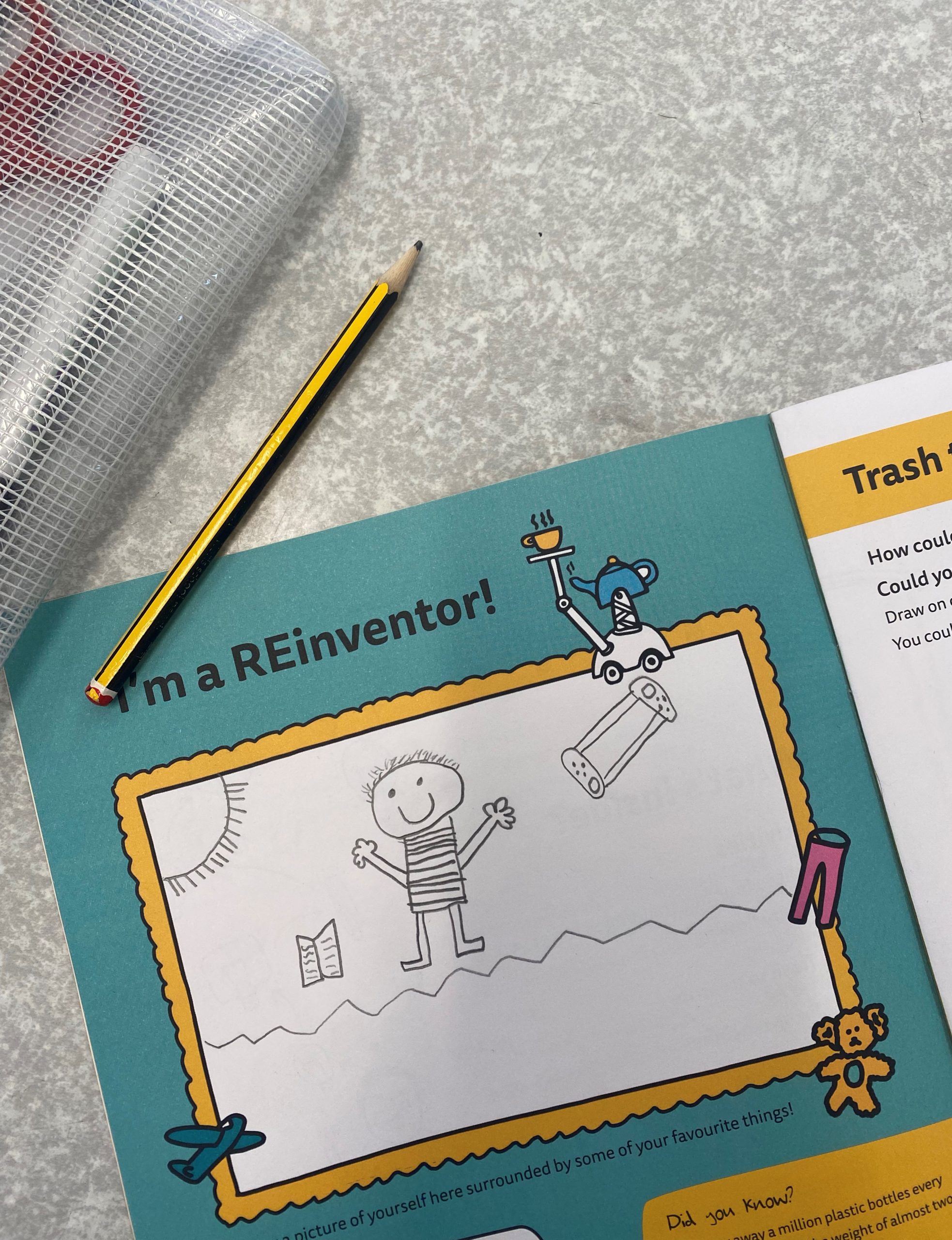 A worksheet titled I'm a REinventor! with a blank drawing space and a stick figure. A pencil and a mesh pencil case are nearby on a speckled grey table.
