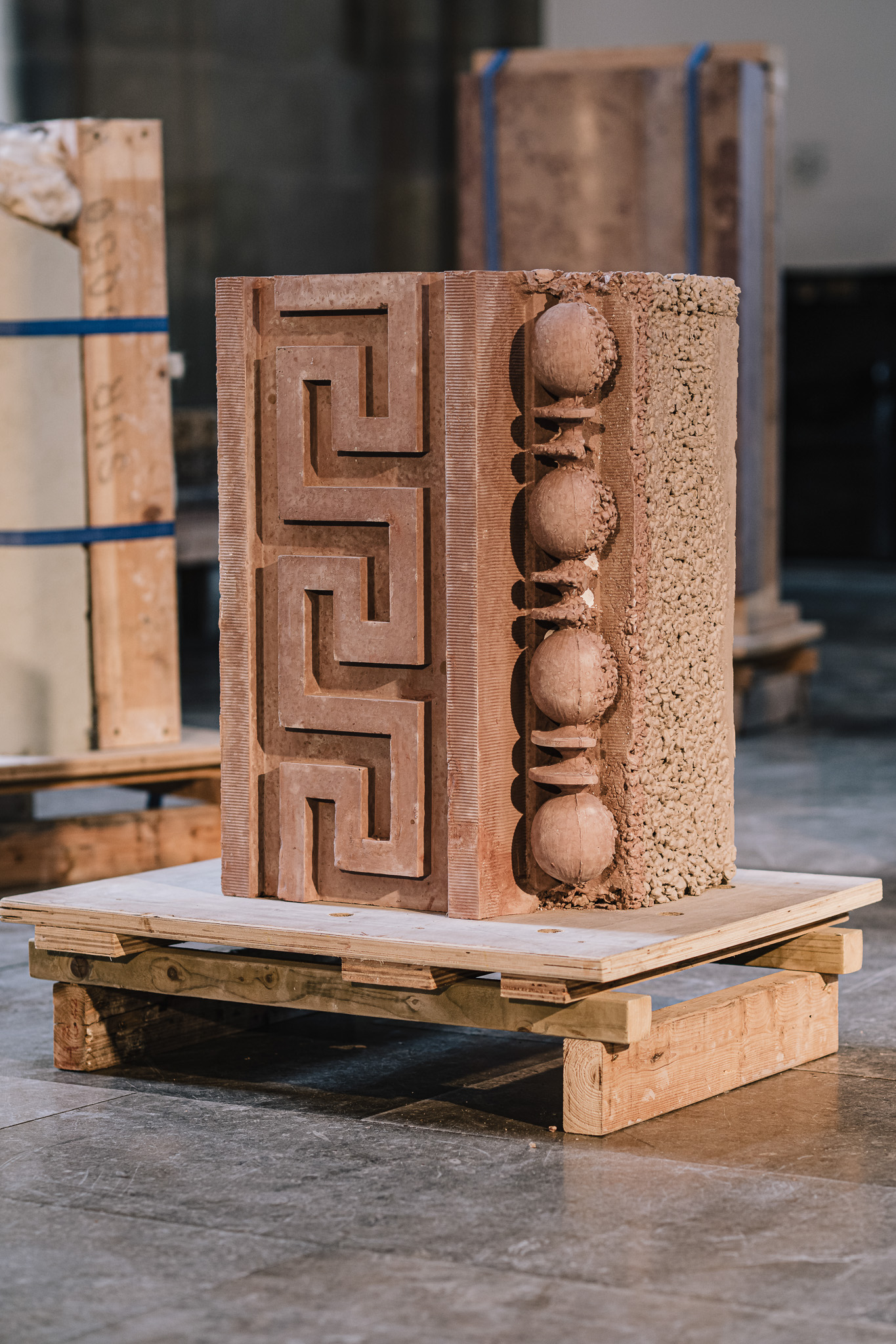 A carved stone block with geometric patterns and round shapes is displayed on a wooden pallet in an indoor setting.