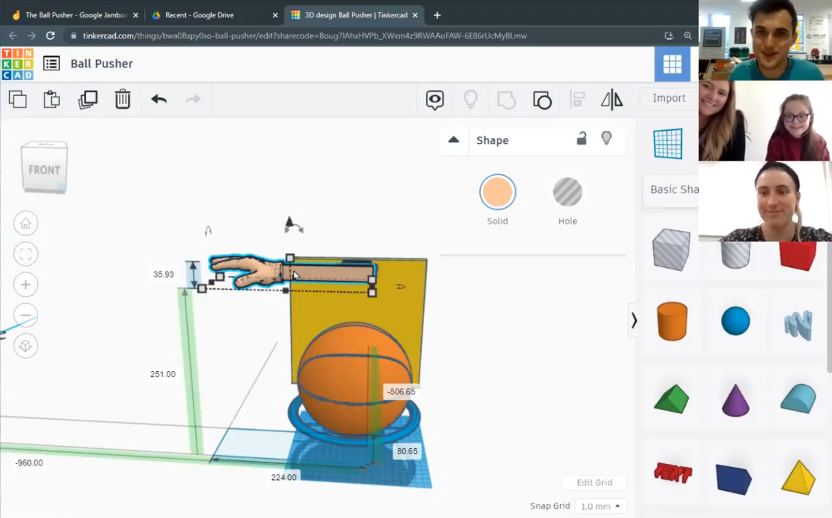A computer screen shows a 3D modelling programme with a hand model above a basketball, a yellow block, and measurement guides. Three people appear in small video chat windows at the top right.