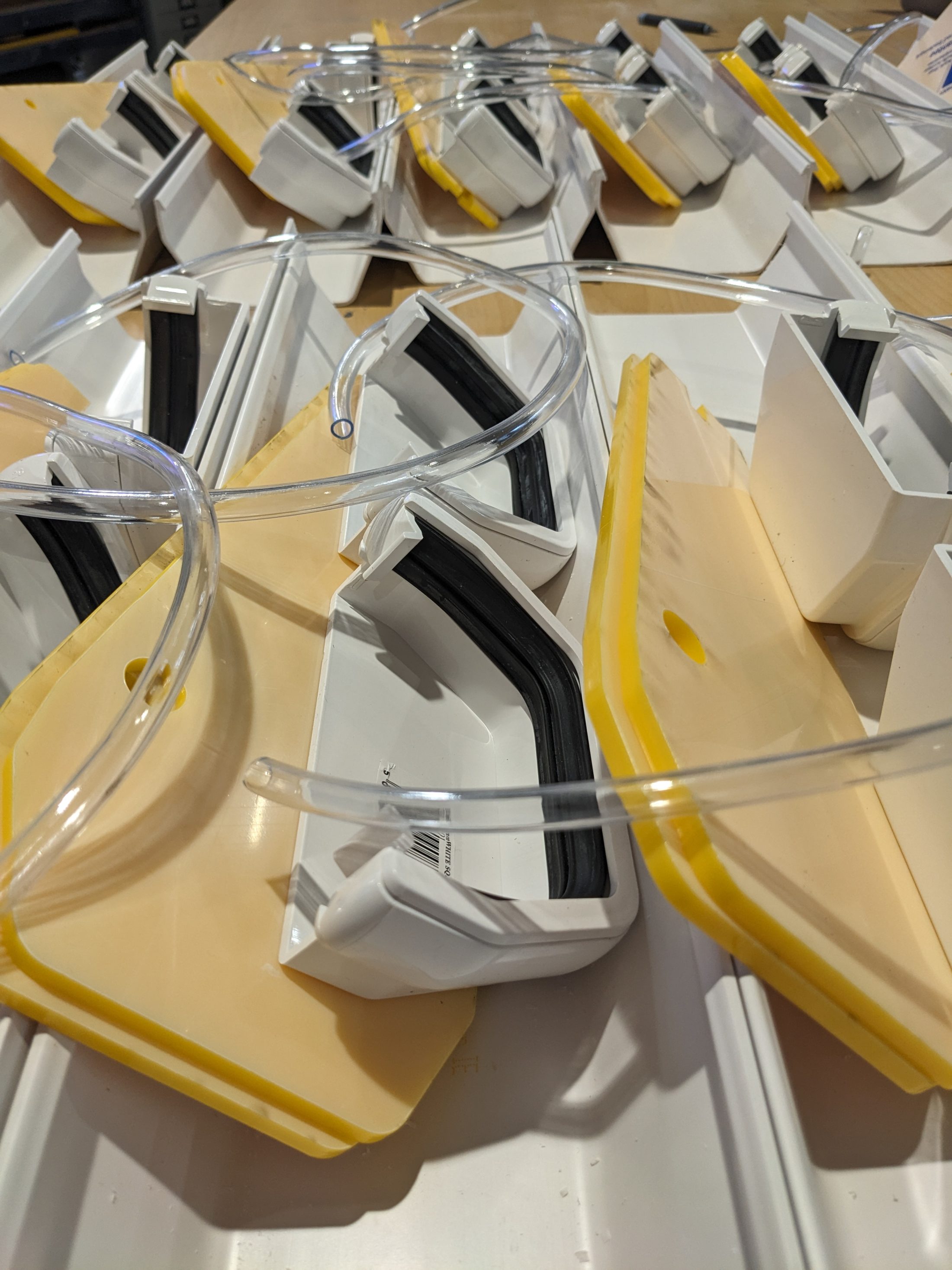 Close-up of several white plastic devices with yellow edges, black rubber strips, and clear flexible tubes, arranged in a slightly overlapping pattern on a flat surface.