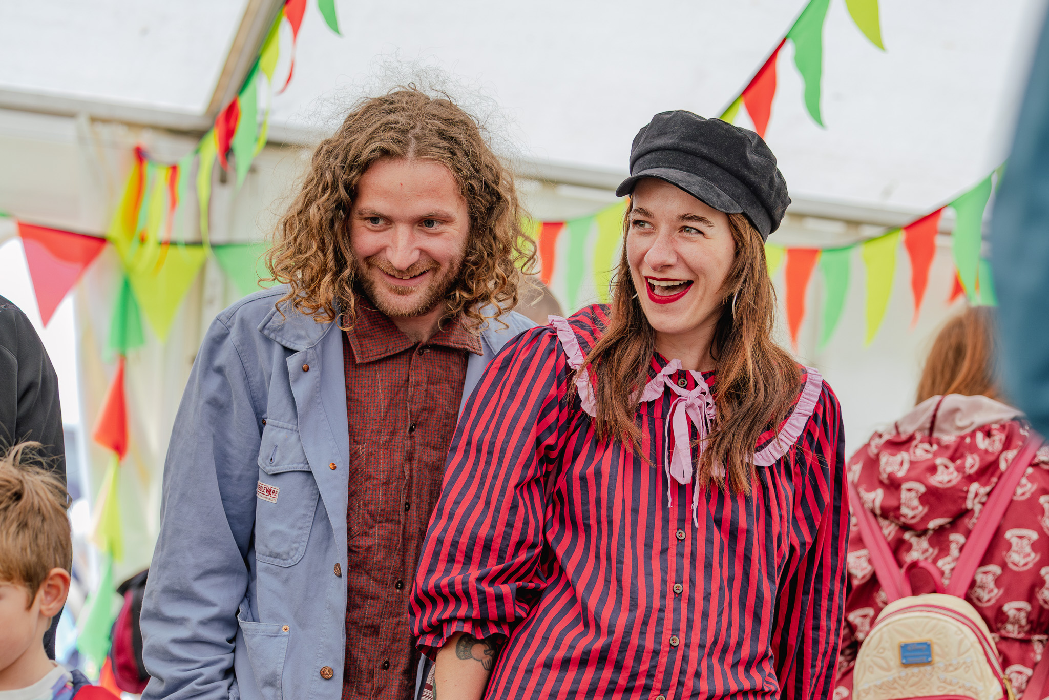 A smiling couple in colourful attire stand under vibrant bunting.
