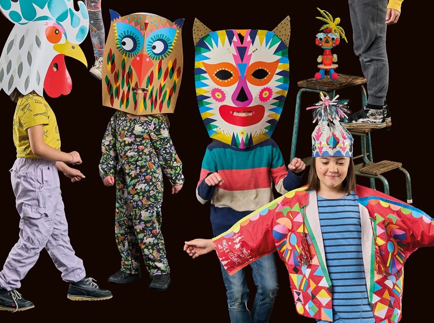 Four children wear bright, colourful animal and fantasy-themed masks and costumes, with one child standing on a chair at the back. The background is solid black, highlighting the festive outfits.