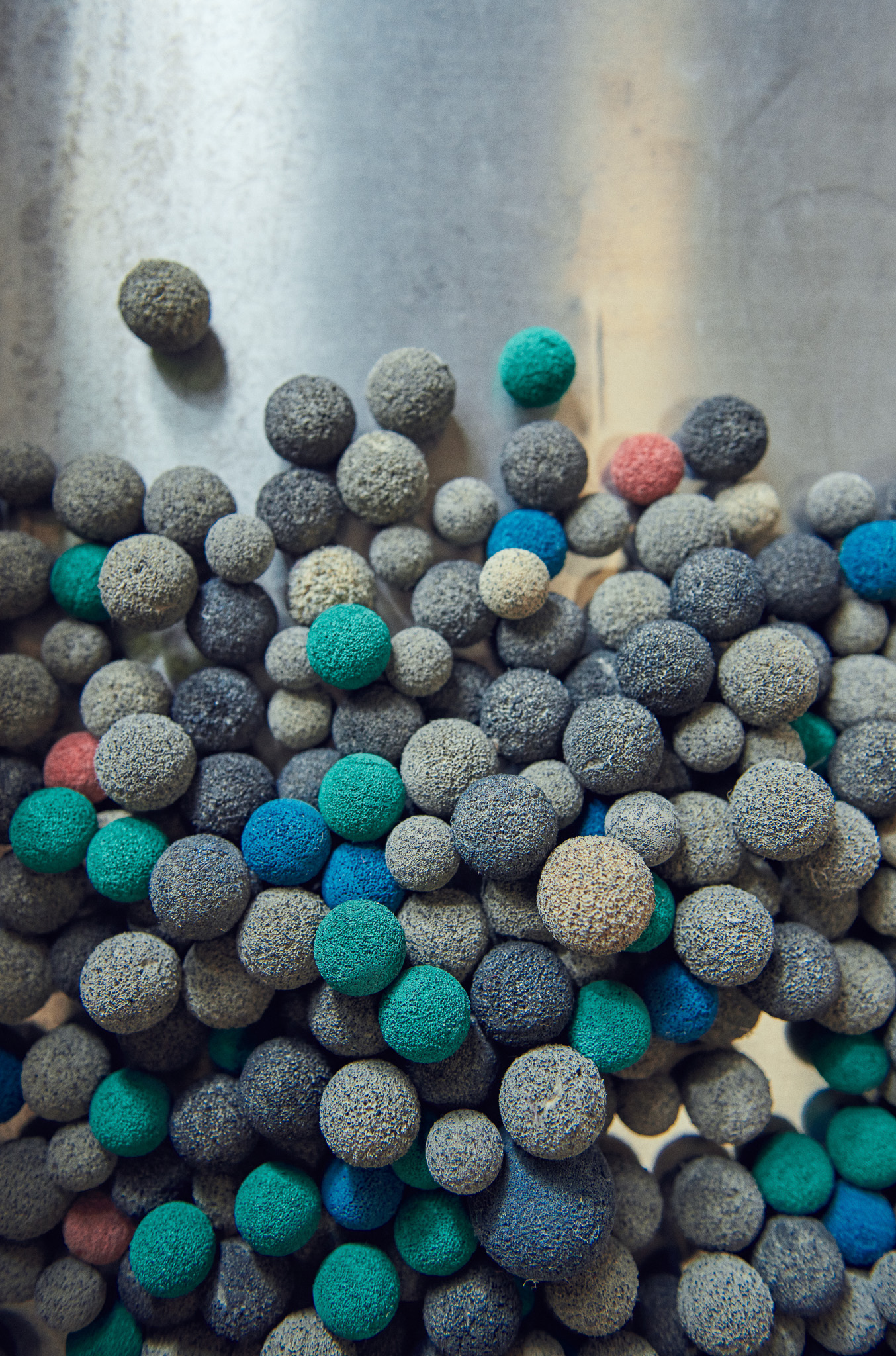 A pile of small, round balls in various colours including grey, blue, teal, pink, and white, resting on a metallic surface.
