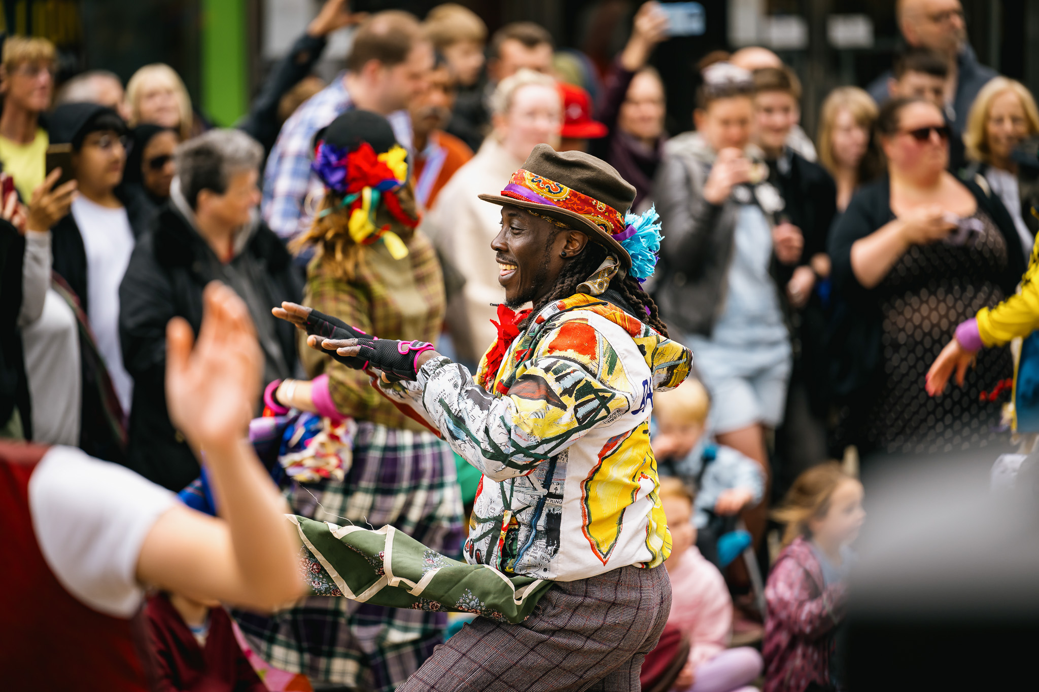 A joyful performer in vibrant, colourful attire dances energetically amid a cheerful crowd.