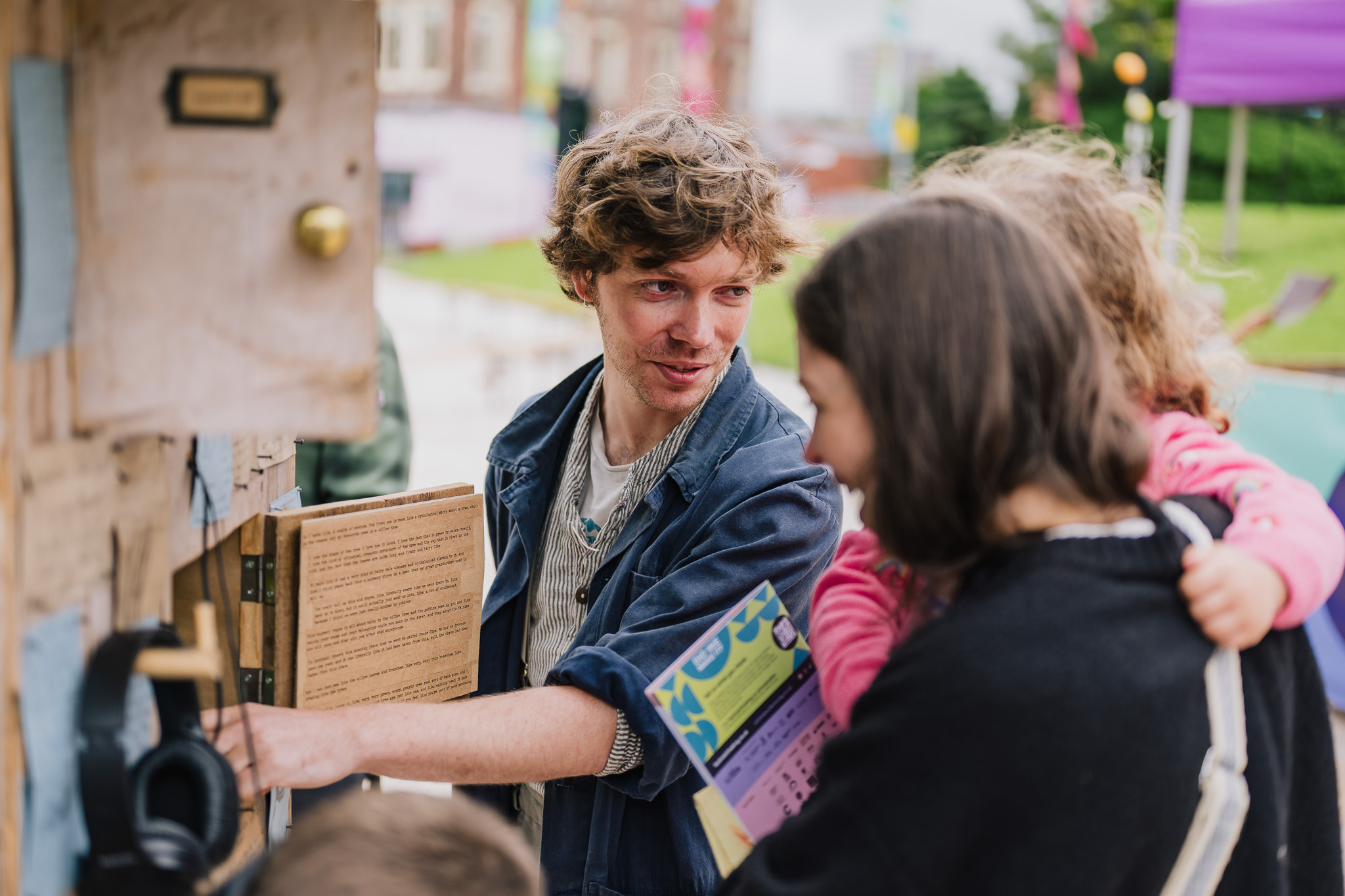 A man shows an art installation to a woman and child at an outdoor event.