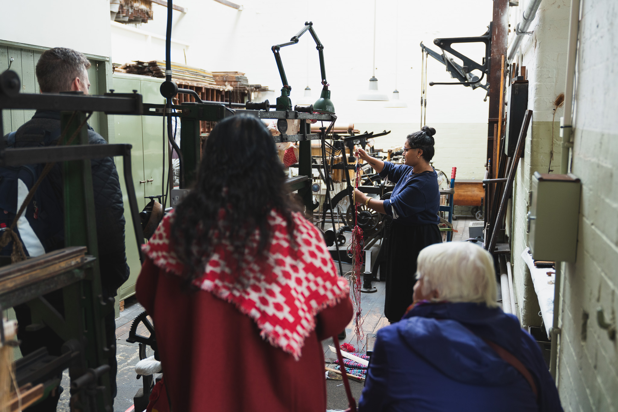 A group of people in a workshop observing Raisa Kabir demonstrating textile machinery.
