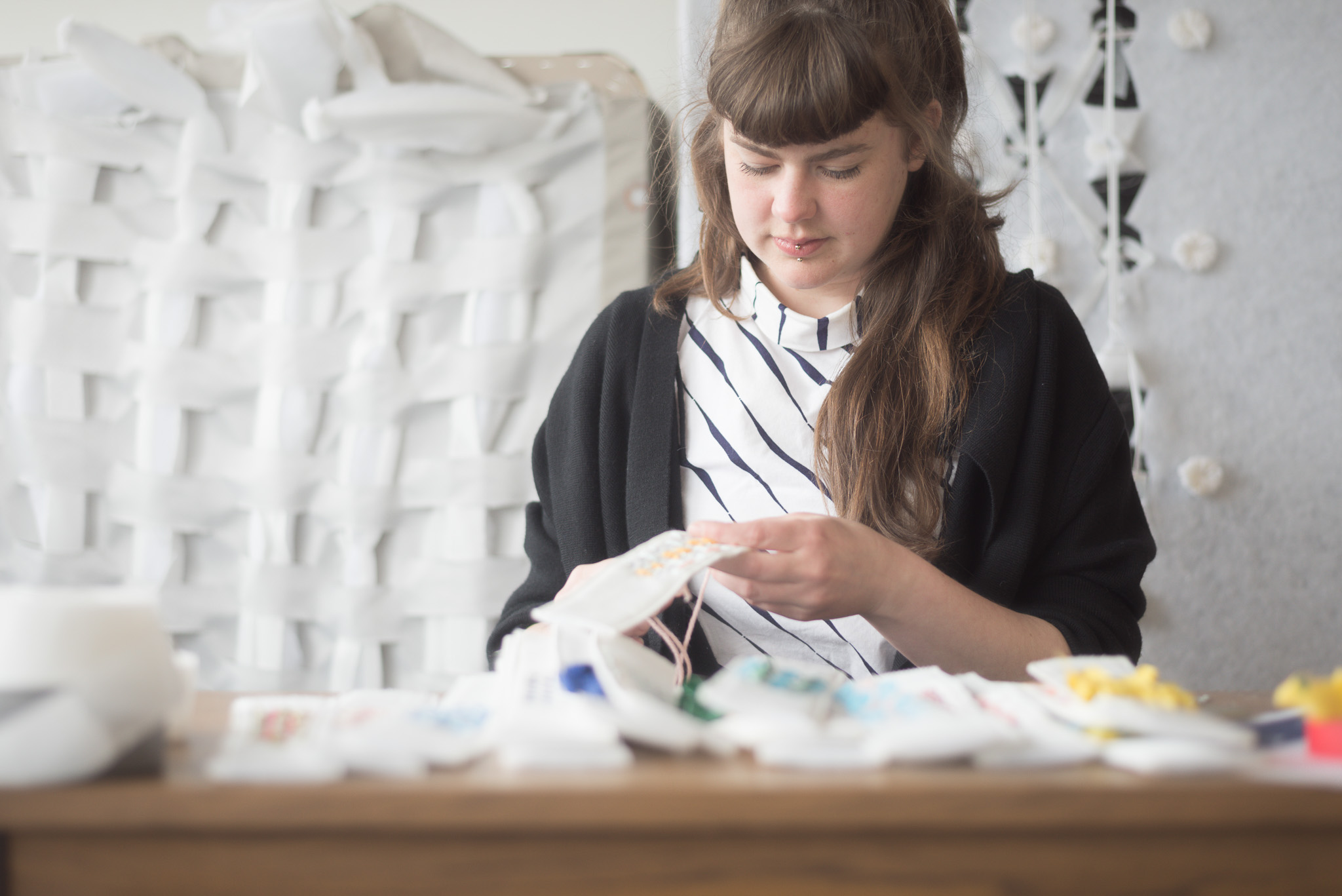 Artist concentrating on a sewing project at a wooden table.