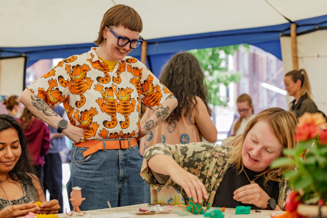 A person in a Garfield shirt smiles and observes others in a workshop at a lively indoor event.