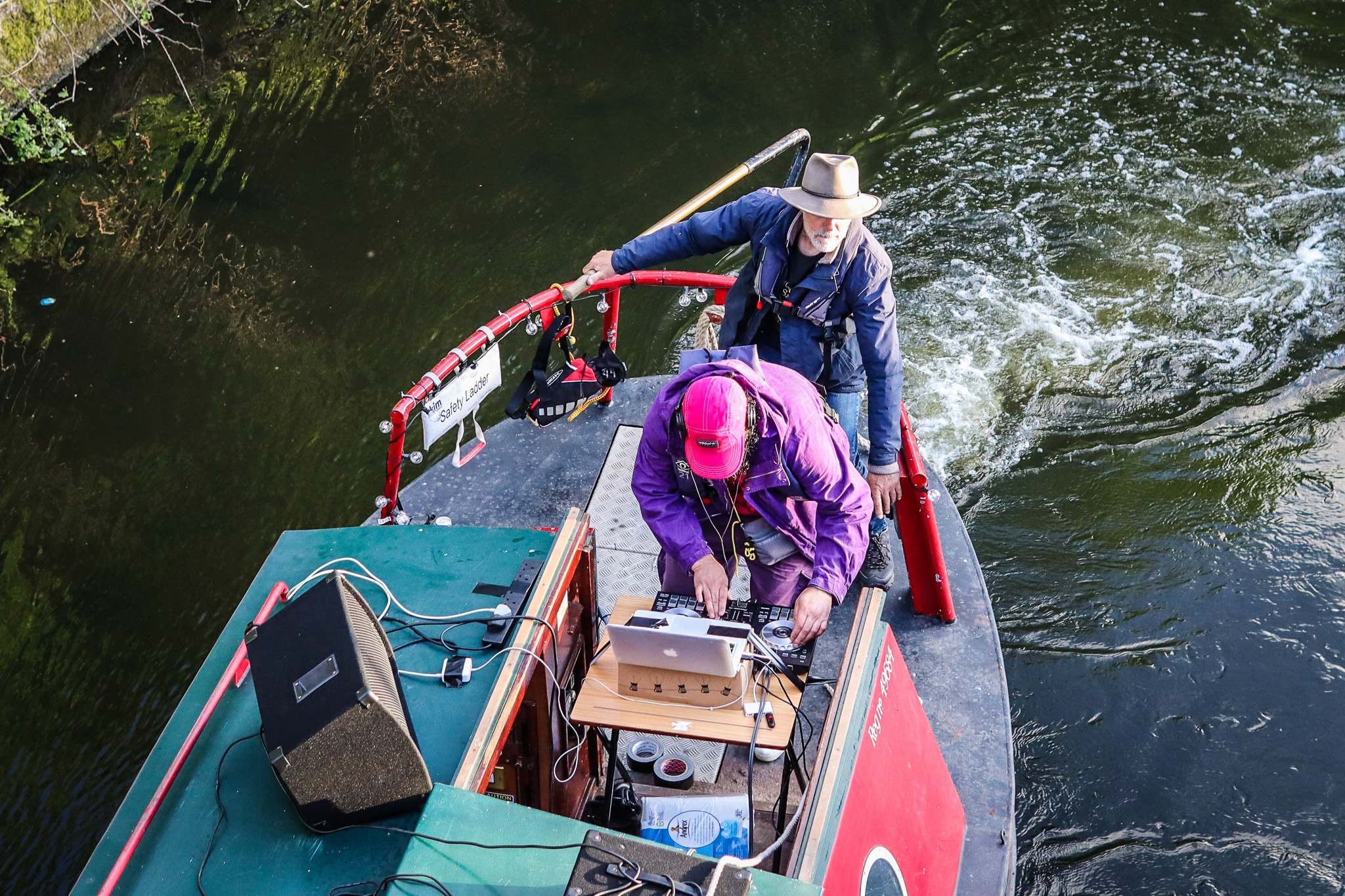 Overhead view of two people on a small boat. One operates sound equipment, the other steers.