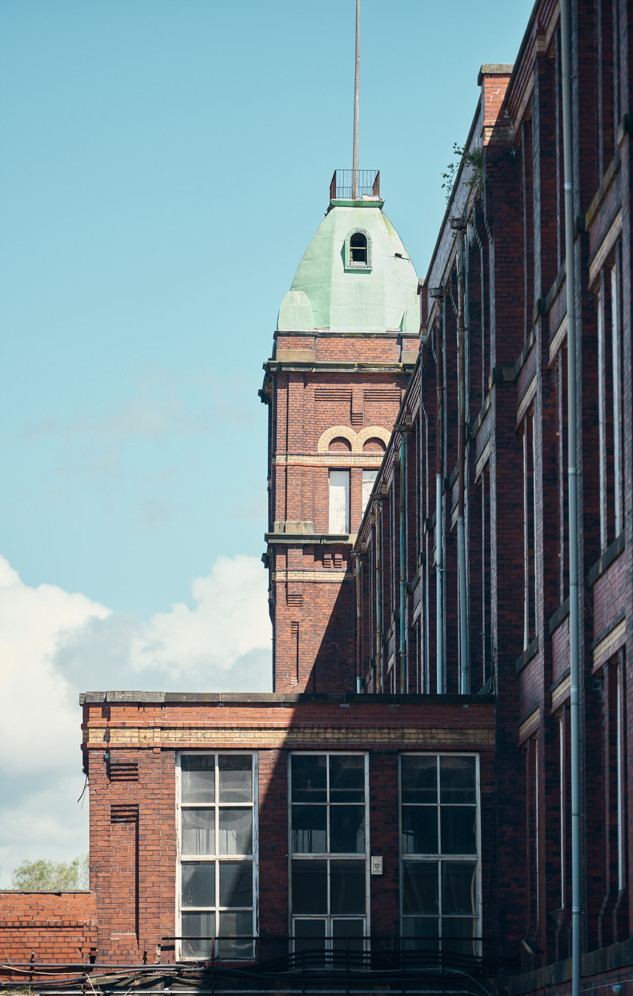 Brick building with a tall green-domed tower under a clear blue sky. The facade is adorned with large windows.
