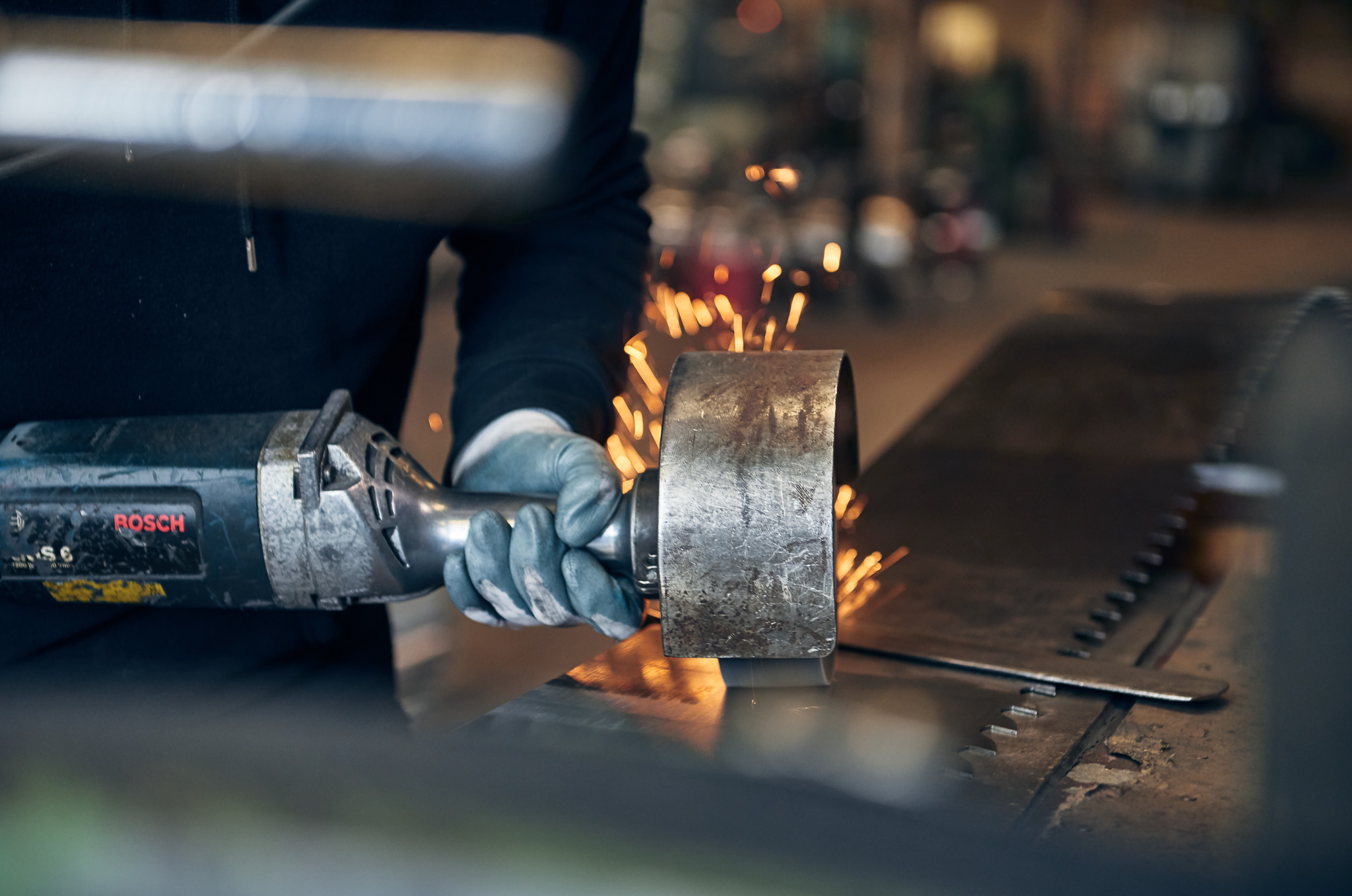A worker in blue gloves uses an angle grinder on metal, creating bright sparks in a workshop.