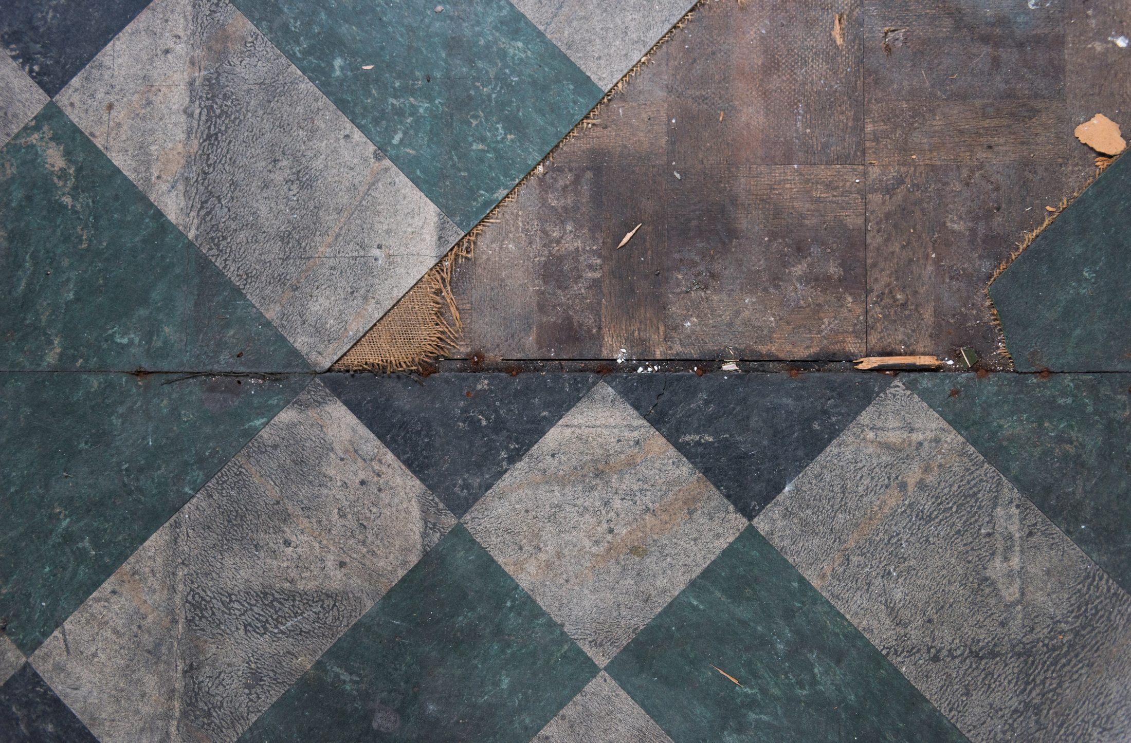 Worn checkerboard-patterned floor in green and gray tones, with visible damage and peeling edges.