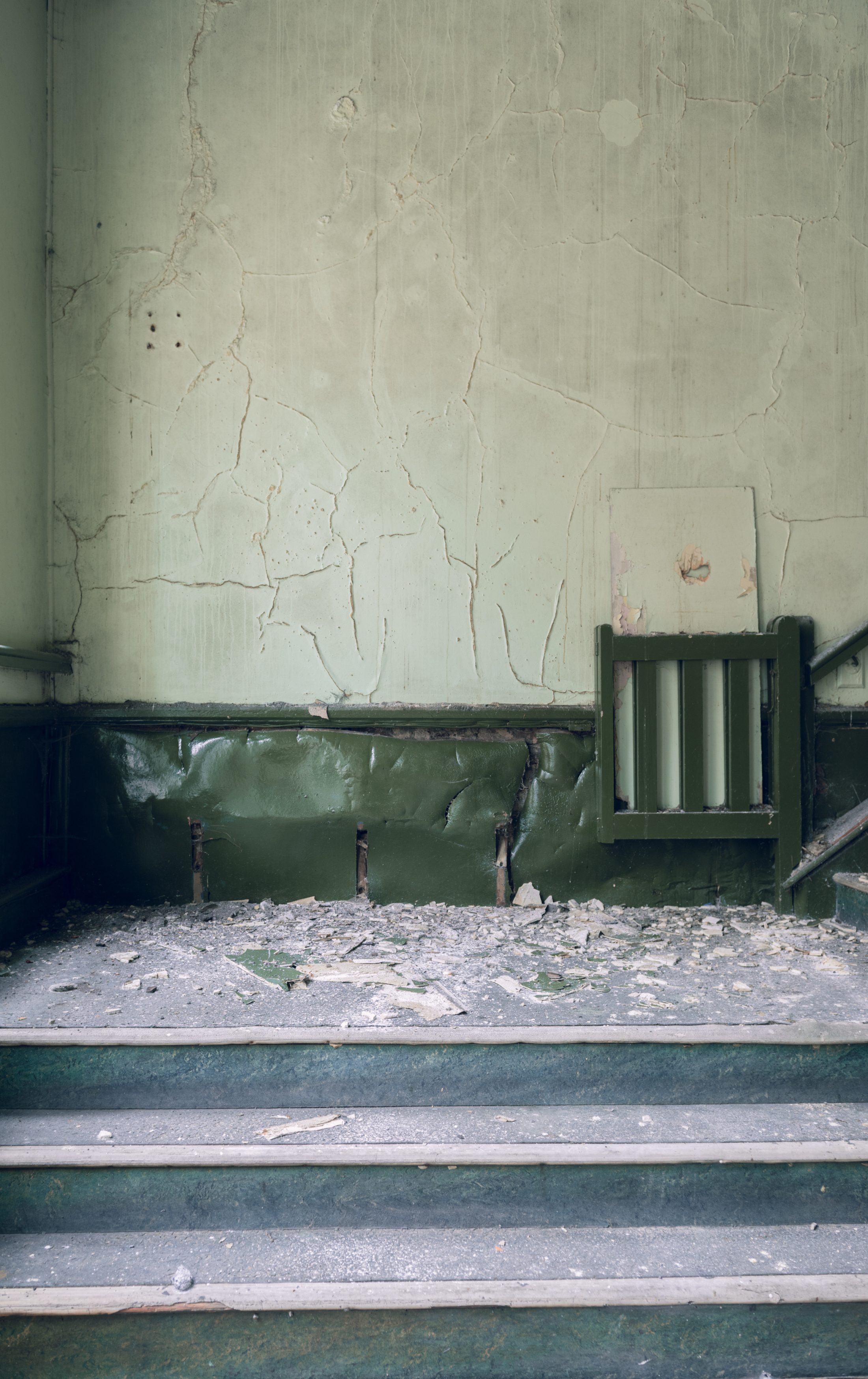 A dilapidated stairway with crumbling steps and a peeling green wall.