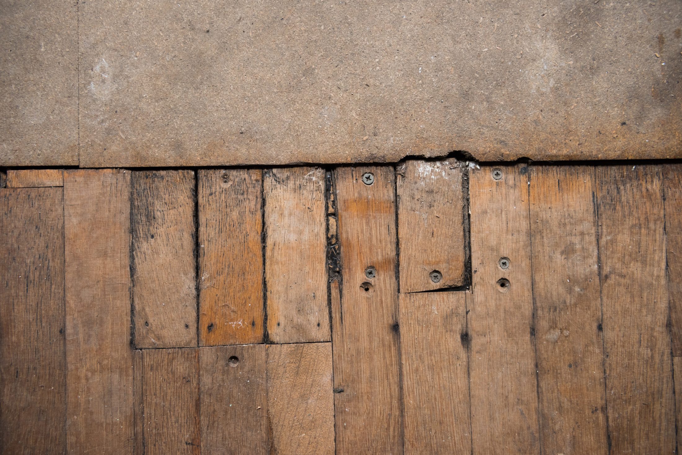 Worn wooden floorboards with gaps and a concrete section above.