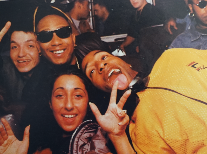 A group of young people smile and laugh together in a van. One wears a RAP beanie, another sports sunglasses, and others make peace signs, capturing a joyful, energetic moment.