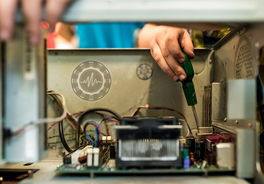 A close-up view shows a person using a green-handled screwdriver to repair the internal components of a computer tower. A circular logo with a wave graphic is visible on the case wall.