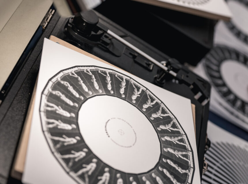 Close-up of printed circular designs with human figures on square sheets placed on record players, resembling old-fashioned animation devices called zoetropes. Other similar patterned sheets are scattered about.