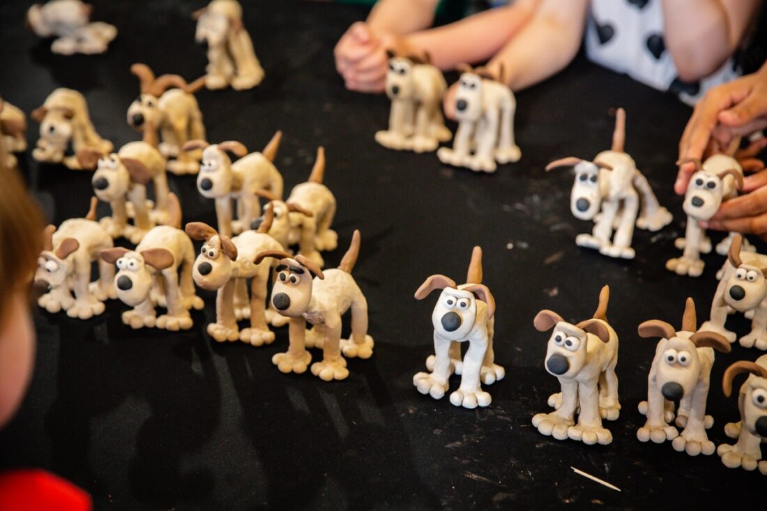 Several small, hand-crafted clay models of a cartoon dog are displayed on a black table, with children's hands visible in the background.