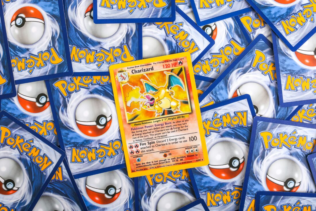 A Charizard Pokémon card is displayed face up among a scattered pile of face-down Pokémon cards, showcasing the character's image and stats.