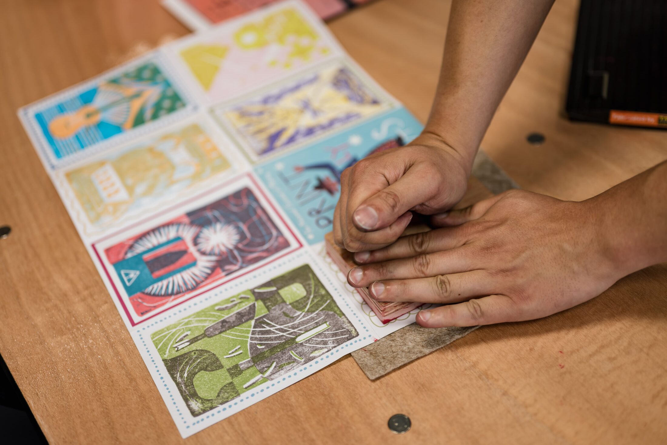A person uses both hands to press down on a colourful card, with several other illustrated cards laid out on a wooden table.