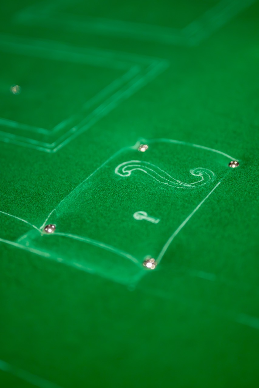 A close-up of a green casino table shows the number 2 outlined in white, along with a small key symbol, and metal studs marking the corners.