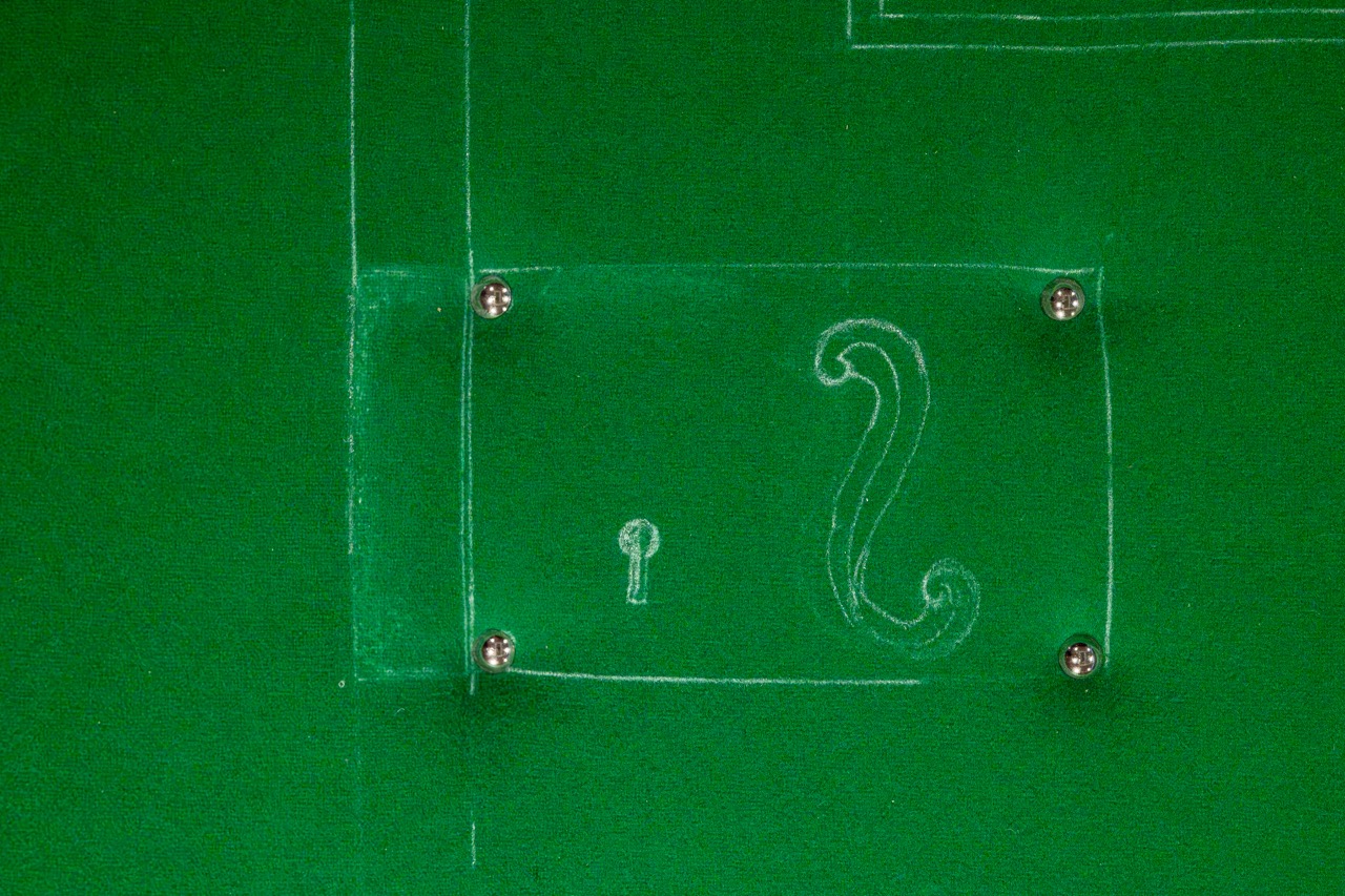 A green surface with a rectangular outline, four metal screws at the corners, a small keyhole symbol, and a decorative question mark drawn in white.