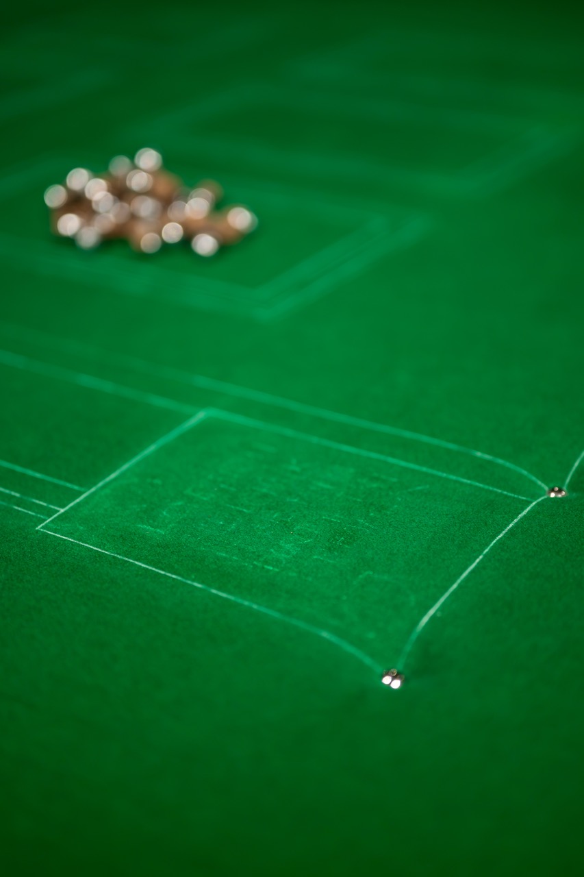 A close-up of a green baize games table with white lines, a pile of small round metallic objects, and a few scattered metal balls, possibly for a casino or board game.