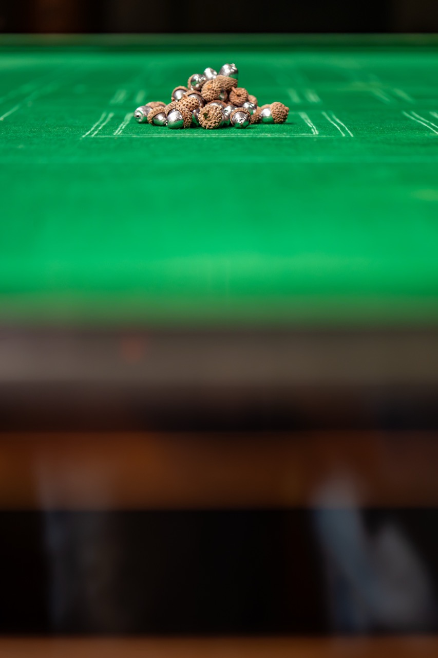 A pile of small brown and silver objects is placed at the centre of a green felt surface, possibly a games table. The background is out of focus.
