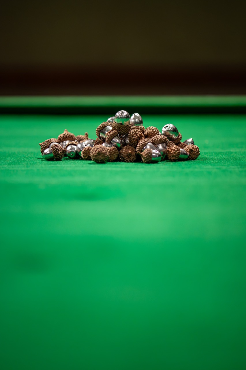 A pile of acorns with metallic tops sits on a green baize surface, possibly resembling a billiard or snooker table, with a blurred background.