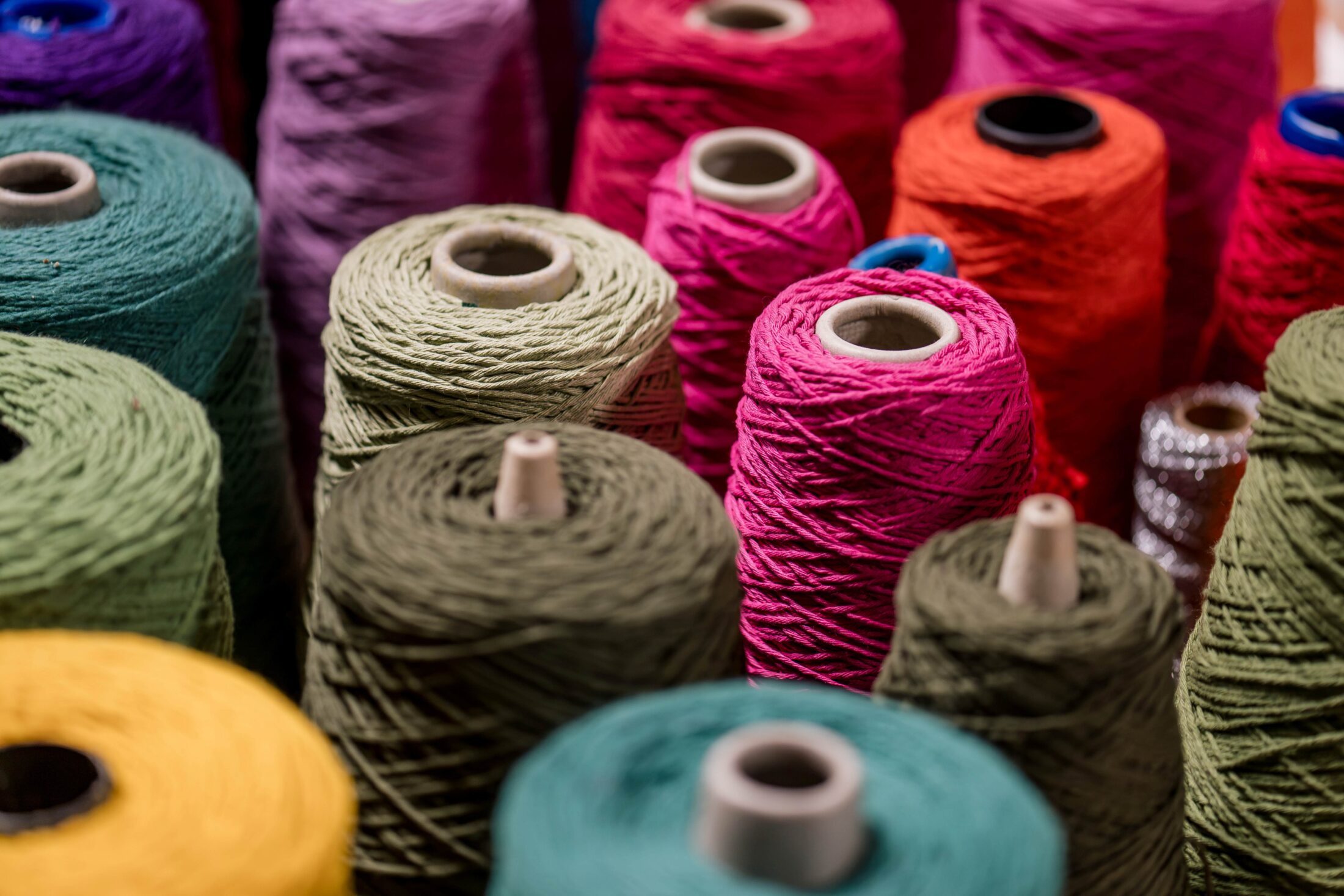 Close-up of multiple colourful spools of thread arranged closely together, featuring shades of green, pink, purple, red, orange, and blue.