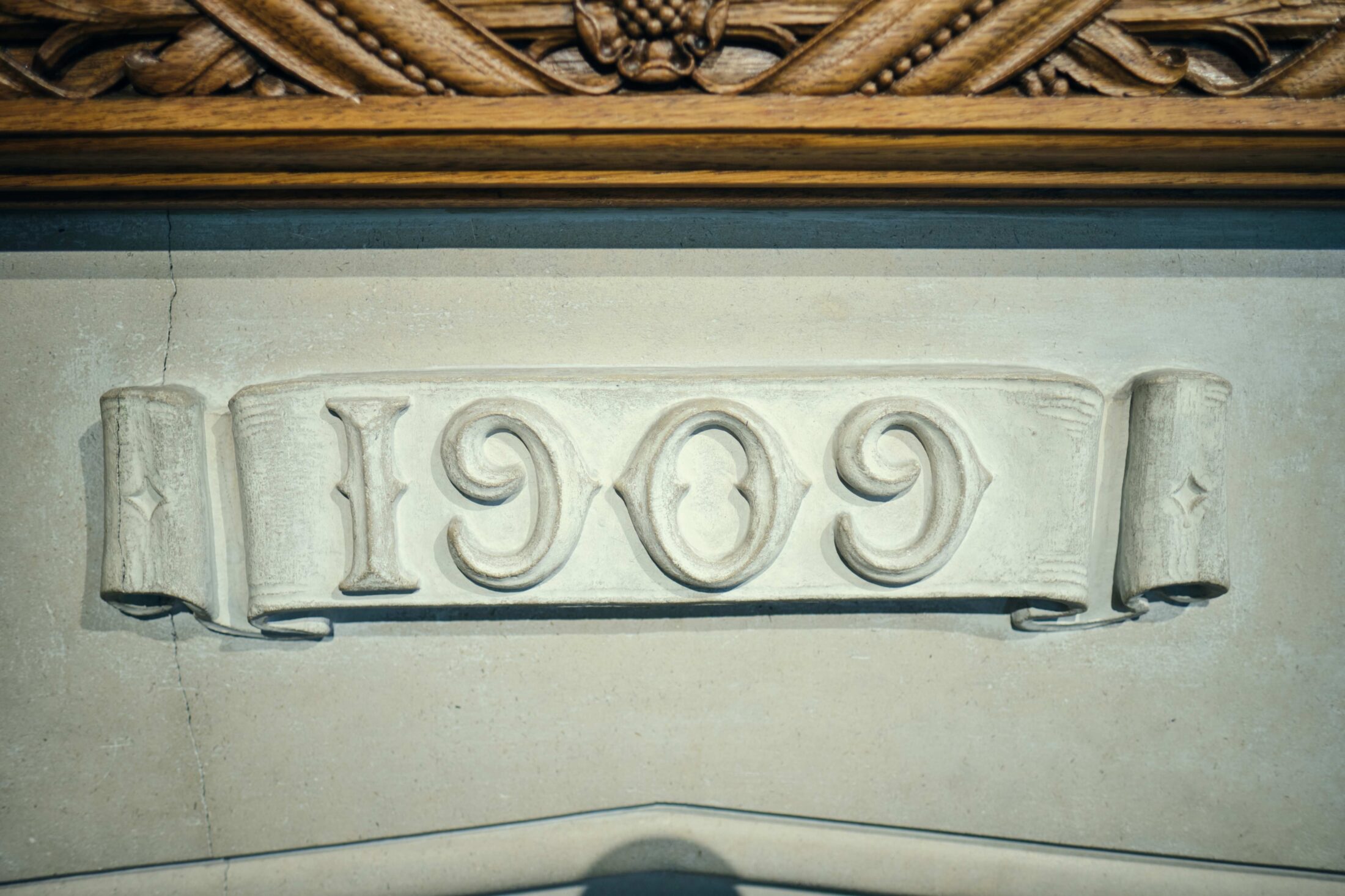 The year 1909 carved into a stone banner mounted on a wall below a wooden trim.