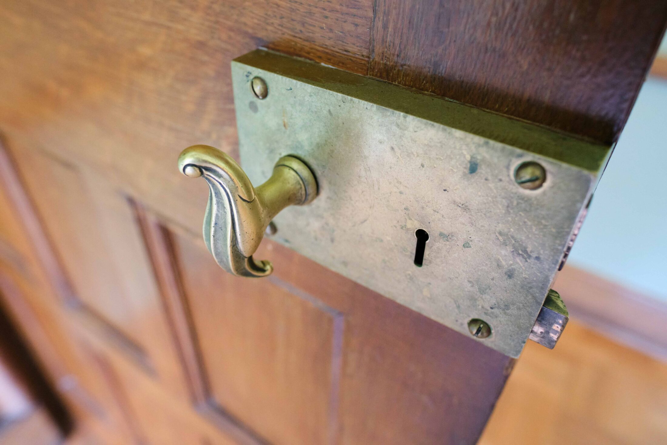 A close-up of a vintage brass mortice door lock with a decorative lever handle on a wooden door.
