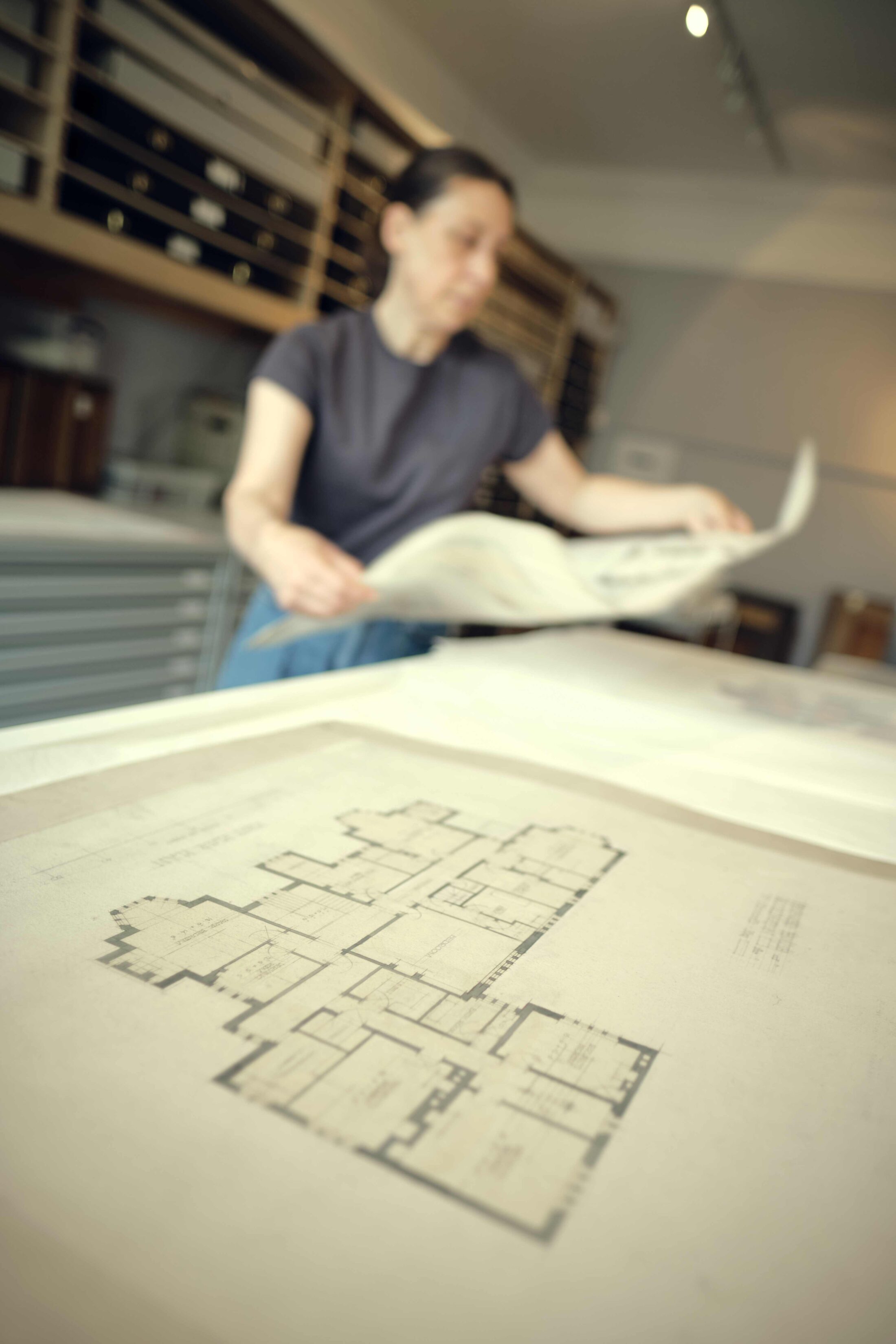 A person in a studio setting examines architectural floor plan drawings.